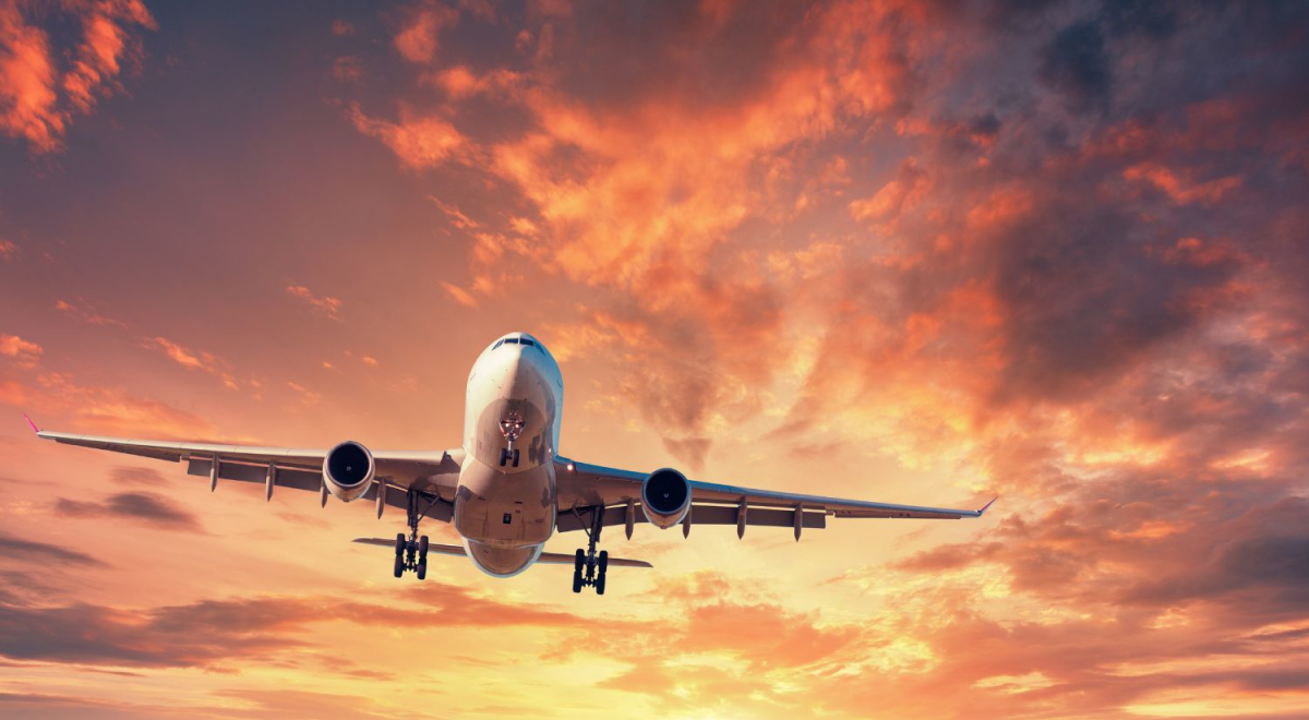 A jet with it's wheels down, coming in to land with a sunset in the background
