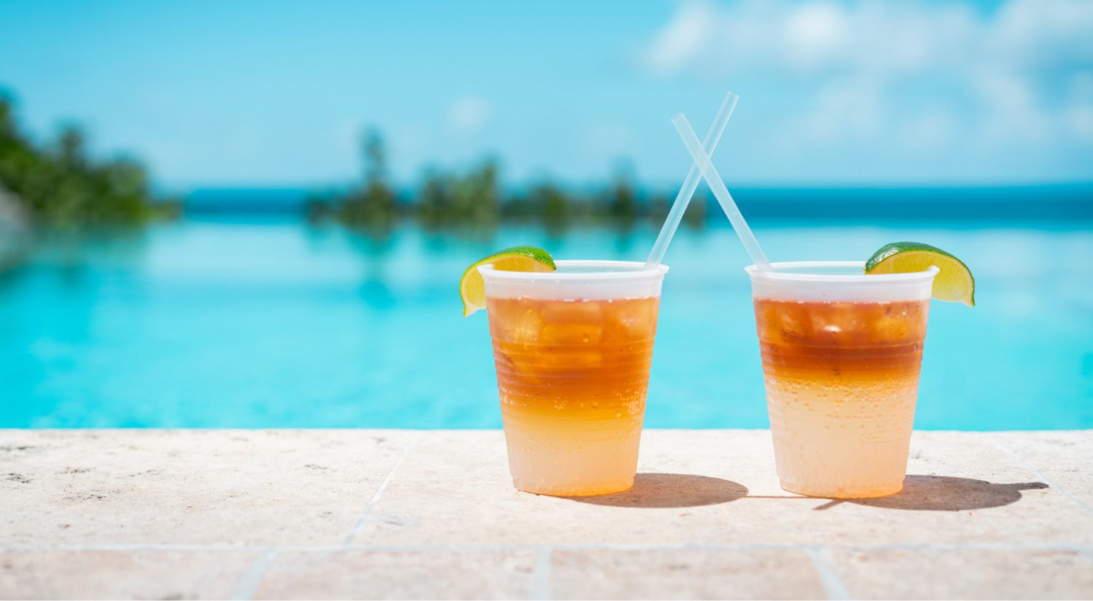 Two glasses of drink sitting next to a pool with beautiful blue water and a stunning blue sky