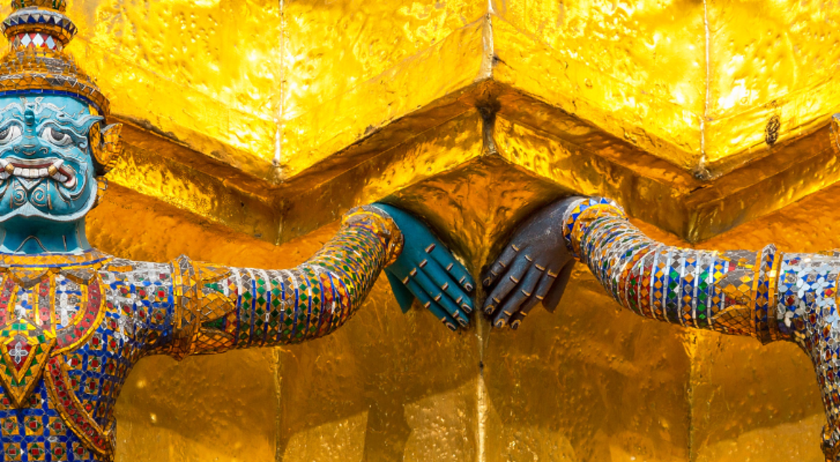 Two statues of traditional Thai gods hold up yellow columns