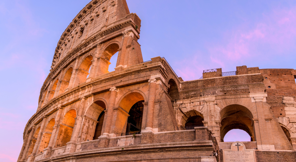 A close up image of the Colosseum. The sky in the background is deep blue and pink showing the sun is setting.