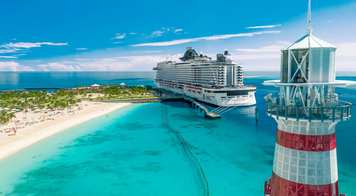 A cruise liner docked at a tropical port with a lighthouse in the foreground