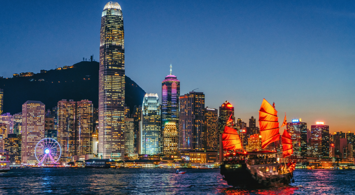 The Hong Kong skyline lit up at night with a bright junk floating on the harbour in the foreground