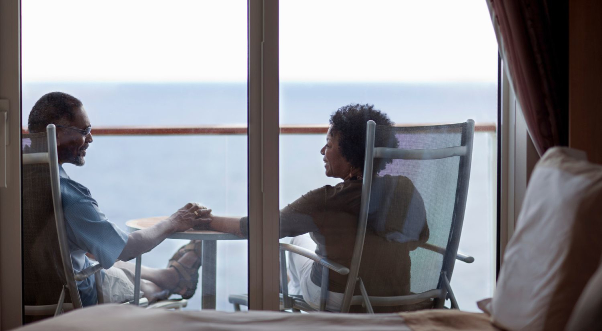 couple sitting on chairs and holding hands on balcony of cruise ship room
