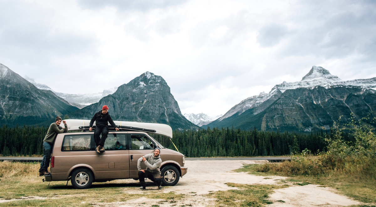 Three male travellers posing with the van they are using for a road trip