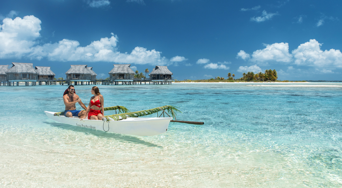 A couple on a boat in Tahiti with overwater bungalows in the background