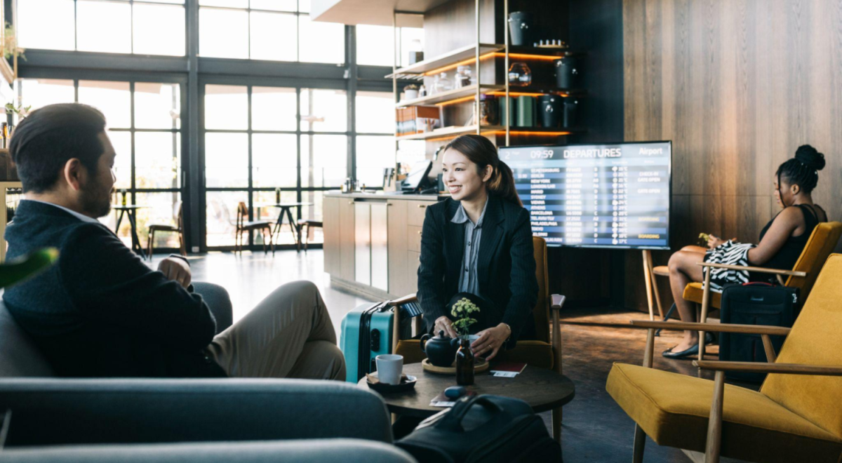 two people in business clothing sit in an airport lounge with coffee on a table in front of them 