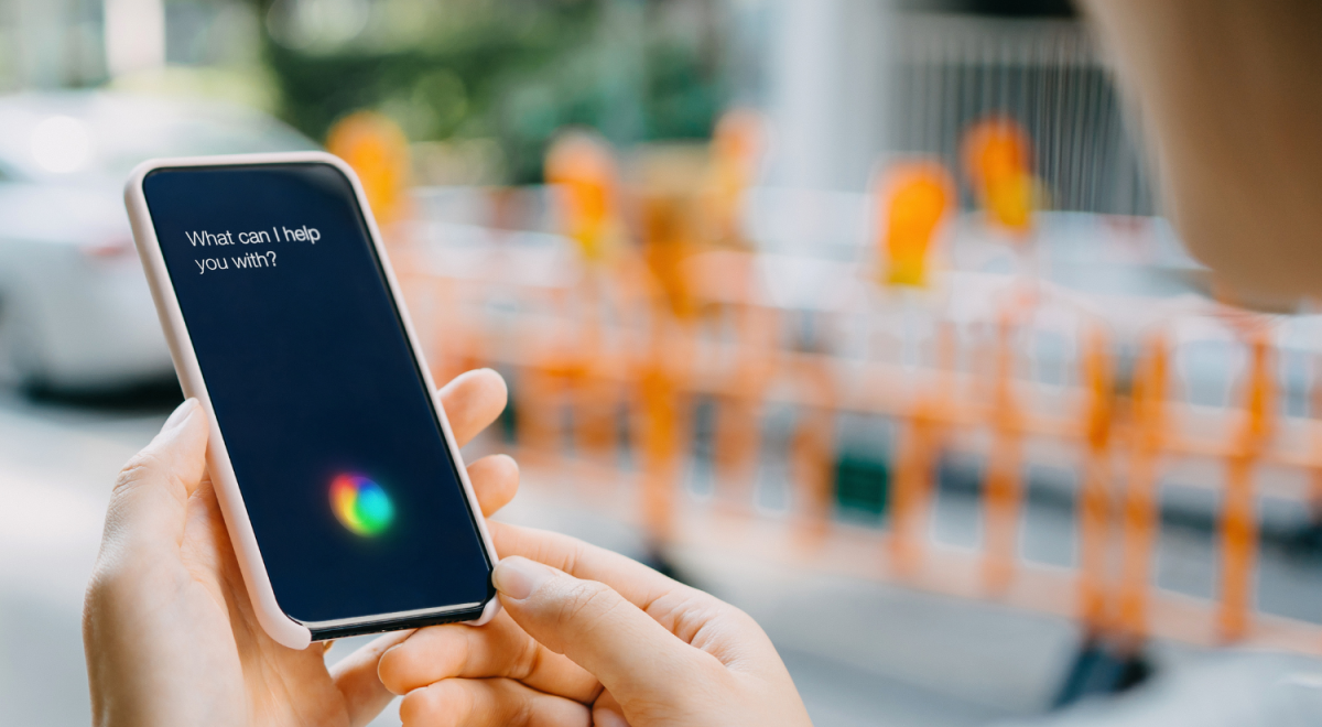 Hands interact with an iPhone with a prompt on its screen saying "What can I help you with?"