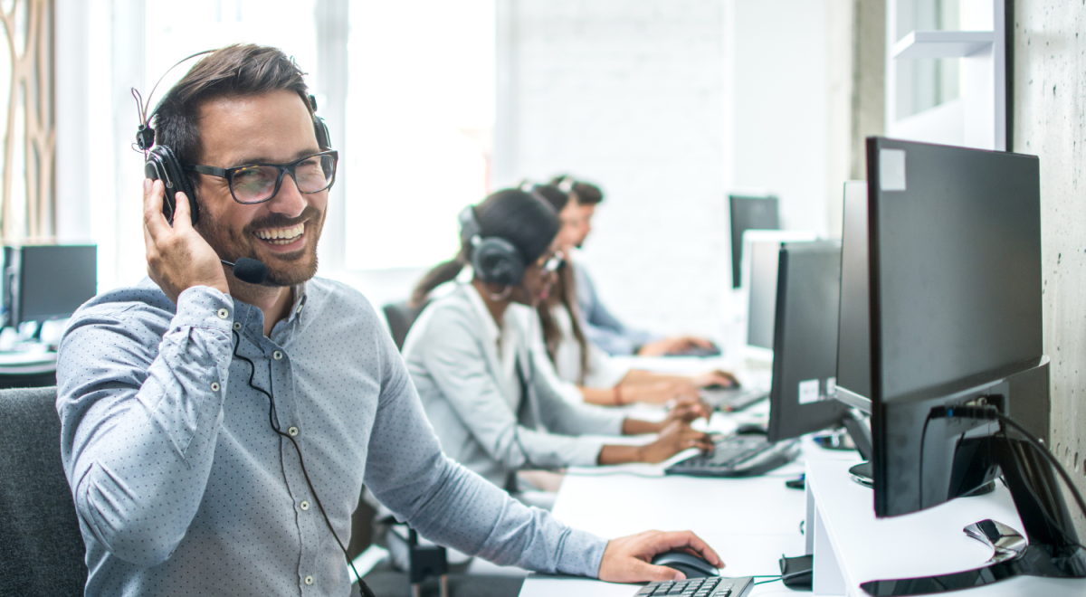 Smiling handsome customer support operator with headset working in call centre.