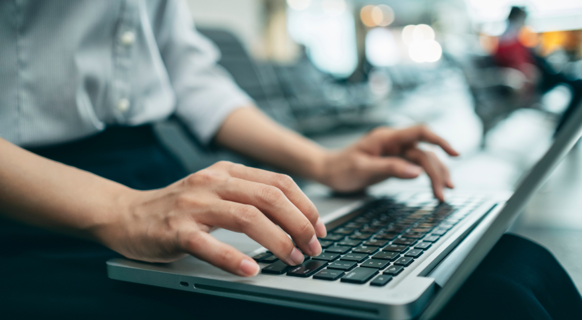 Hands work on a laptop at an airport