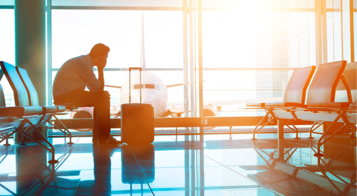 Stressed businessman sitting with his suitcase in an airport terminal watching a delayed flight