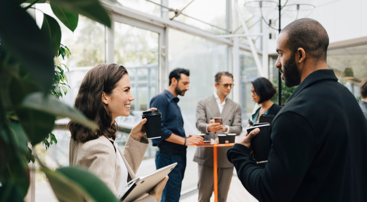 Business professionals networking and chatting over coffee in a bright, plant-filled event space