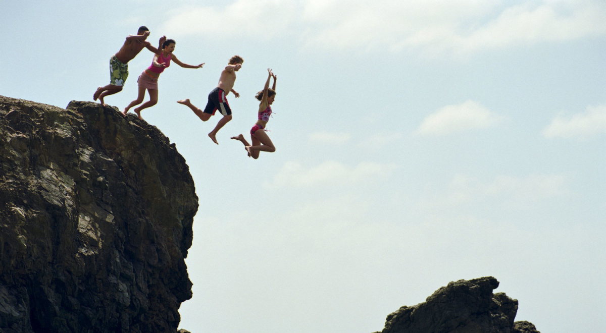 Group of friends jumping into ocean from rock cliff