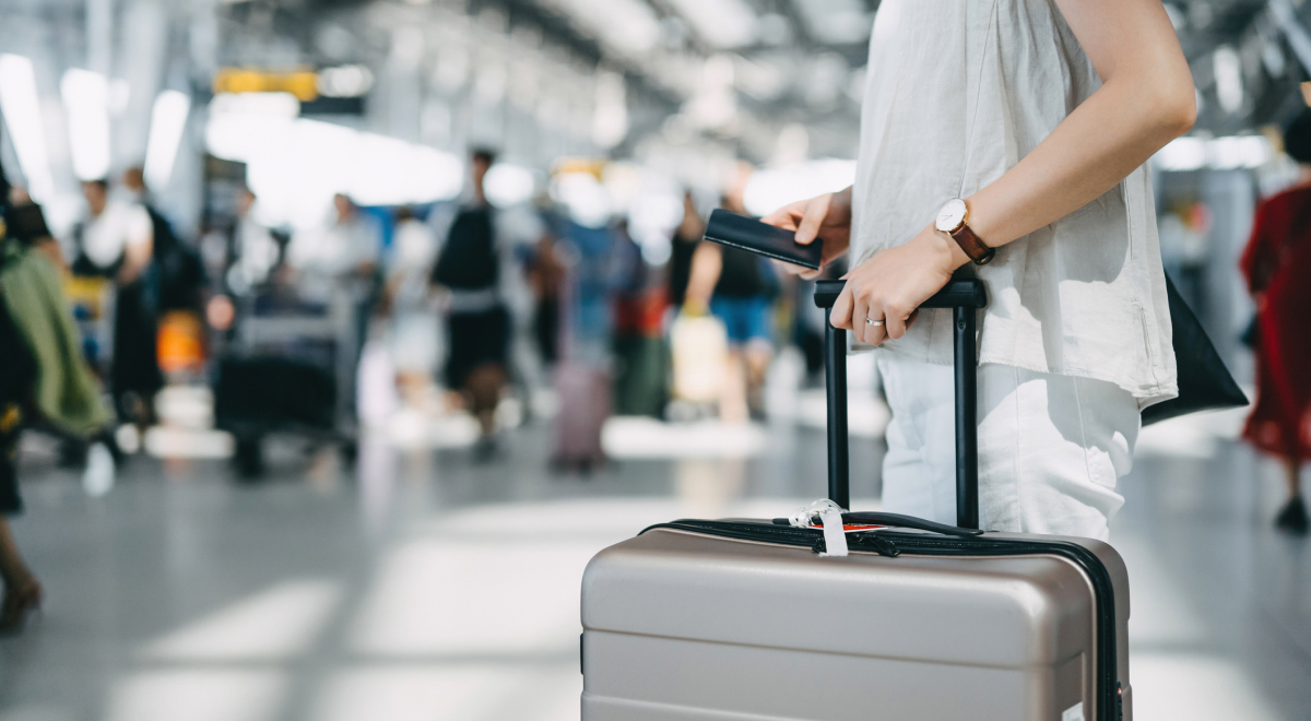 woman standing in airport terminal holding a suitcase