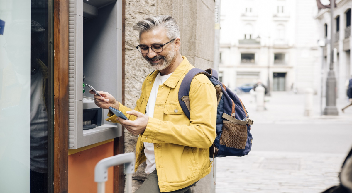 Man looking at phone and taking money out of an ATM