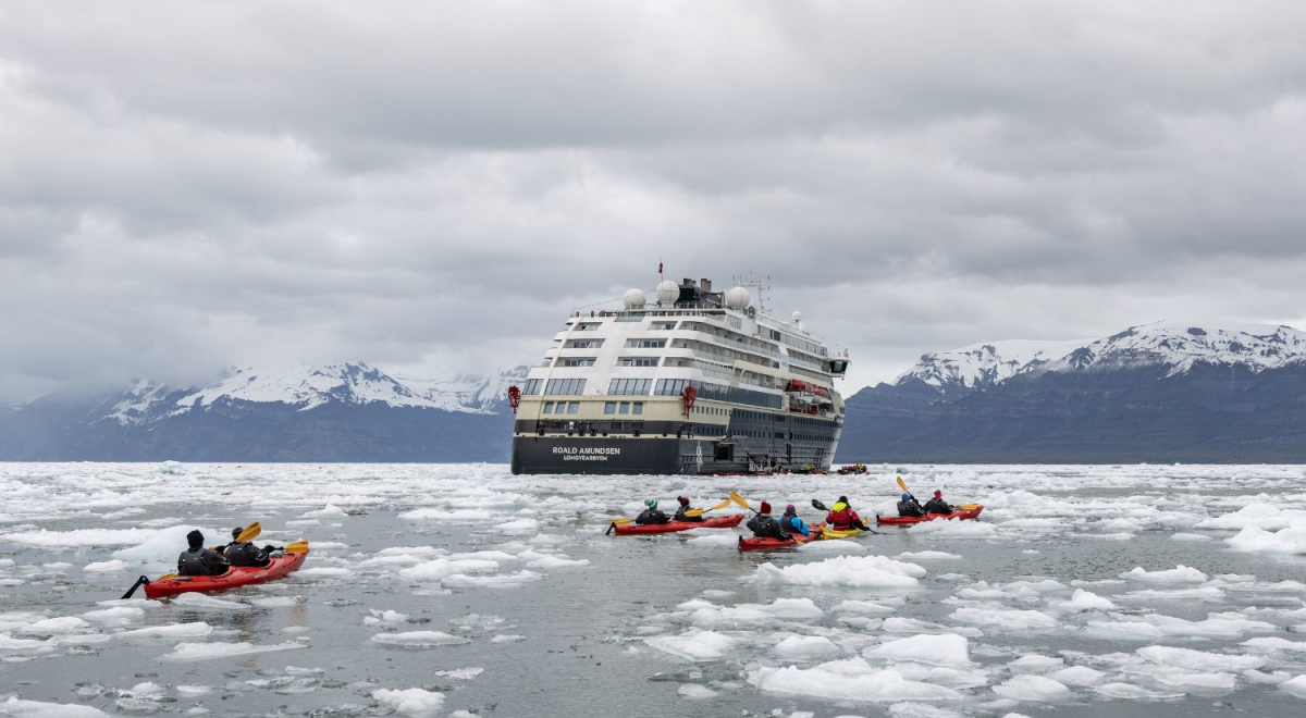 A ship in icey waters. People in canoes are paddling arounding in the foreground exploring. 