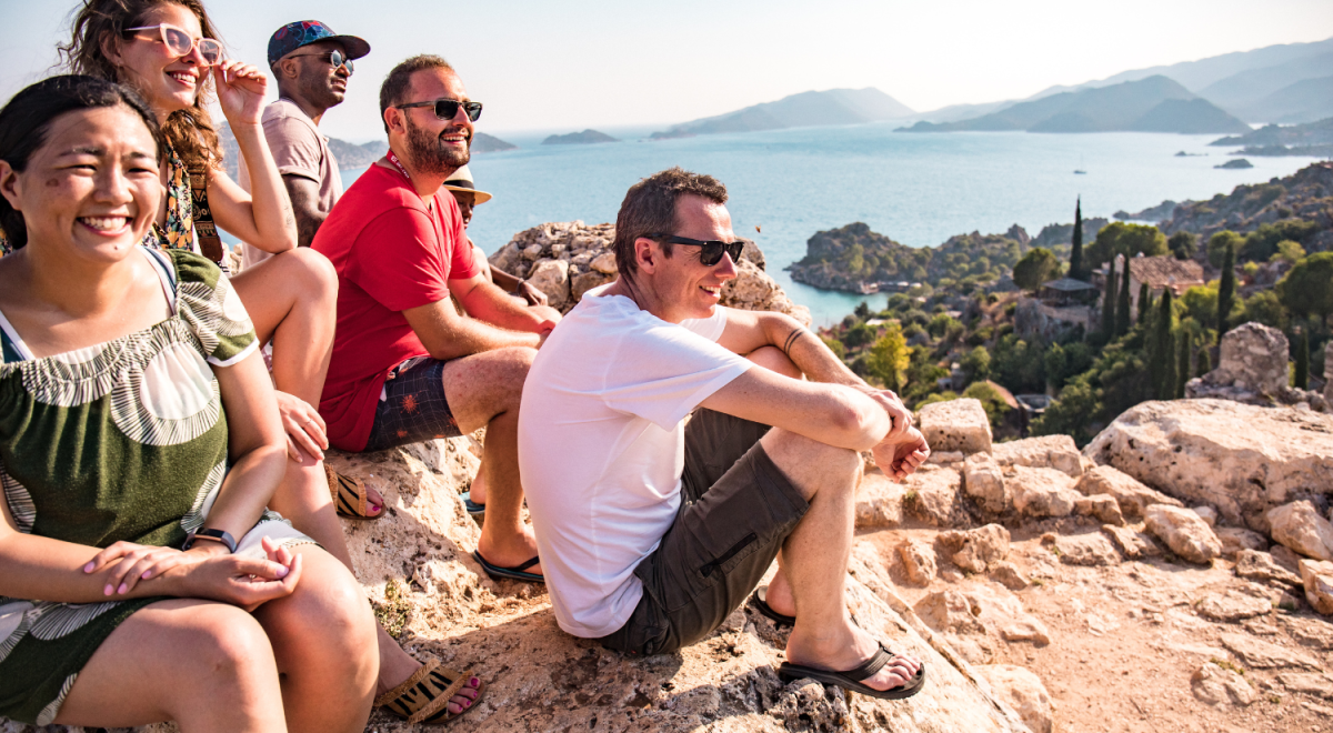 A group of travellers sit smiling looking out at the ocean from a rock