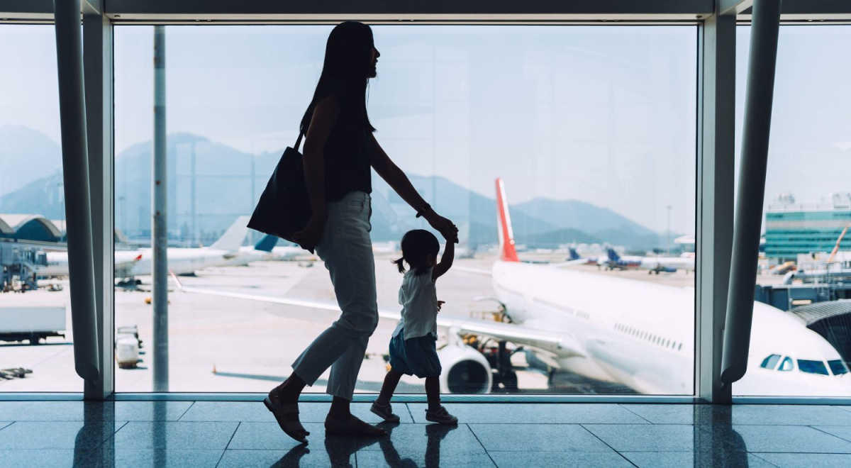 A mother holding her young child's hand walking through an airport