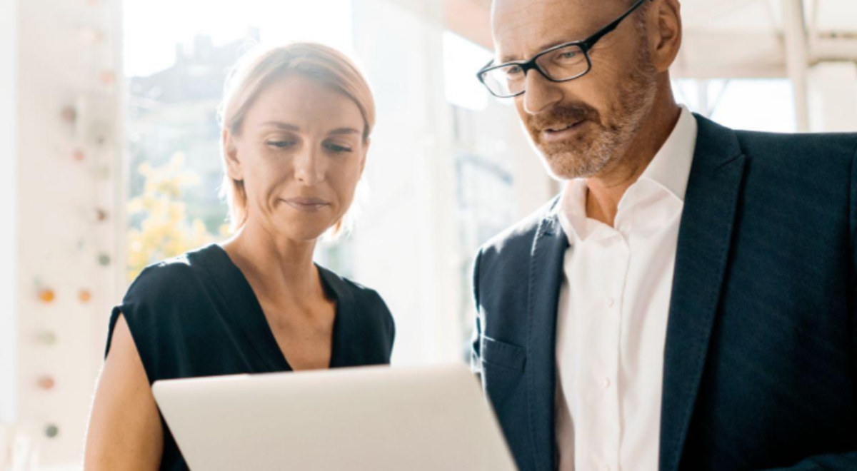 man and woman standing using laptop