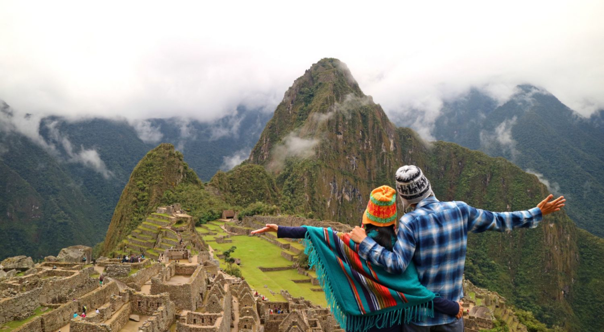 A couple with their arms out overlooking a view of Machu Picchu
