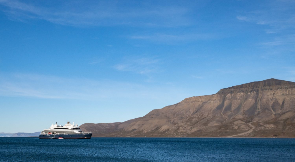 A small cruise ship in the water with rugged mountains in the background.
