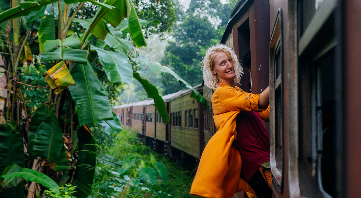 Woman on the edge of a train going through a lush rainforest