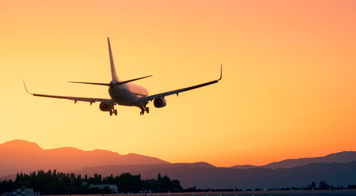 A plane coming in to land with a bright yellow sunset in the background