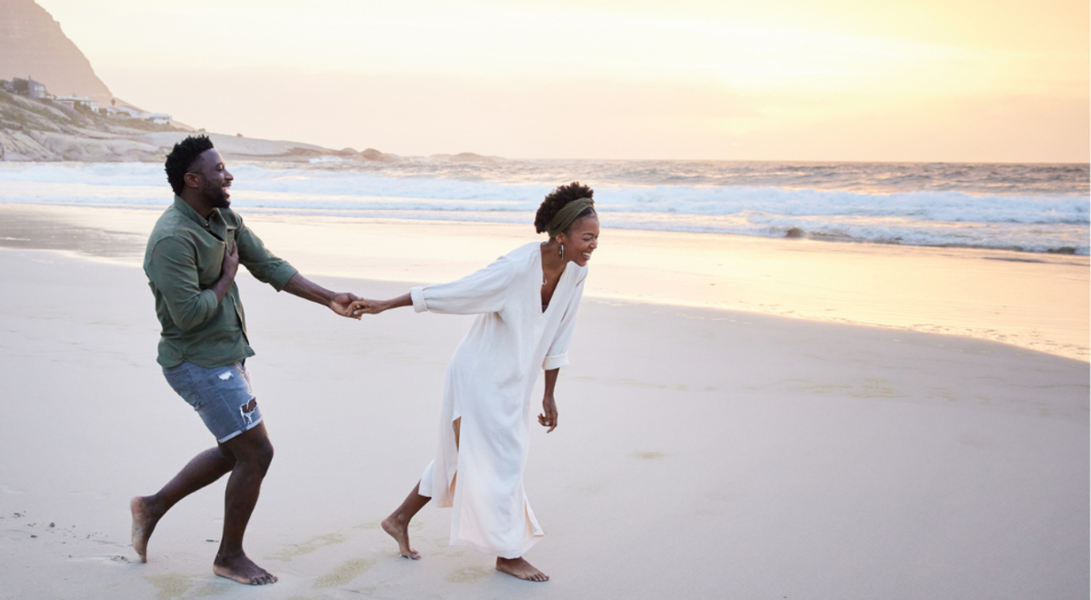 Couple running and laughing while holding hands on beach at sunset