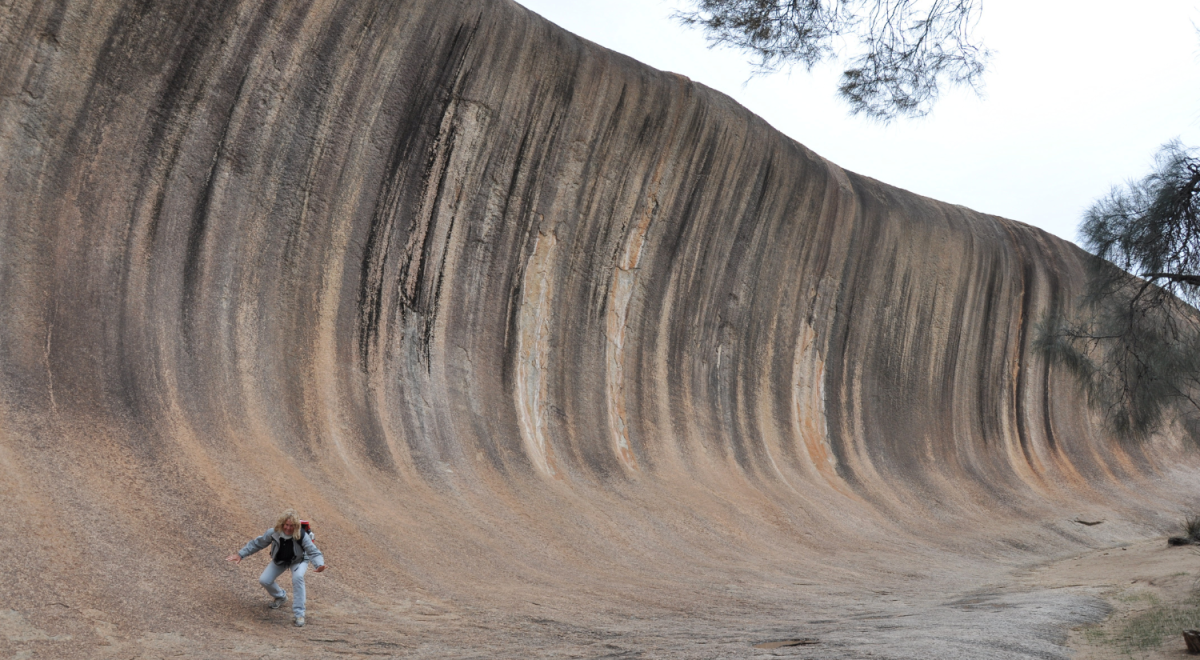 A person mimes surfing down the tall face of Wave Rock