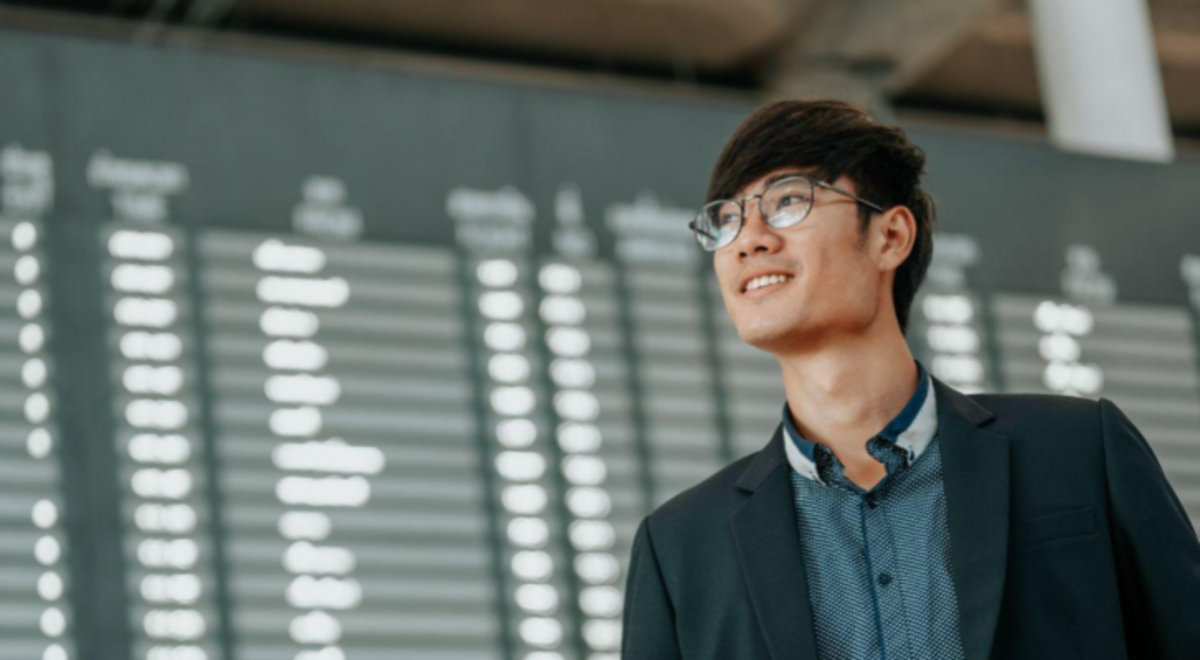 man smiling in front of airport billboard