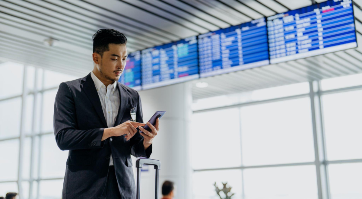 Man standing in airport tapping his phone