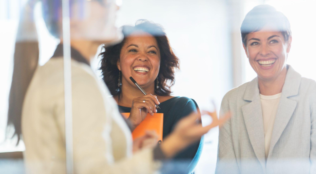 two business women smiling as they watch other lady speak