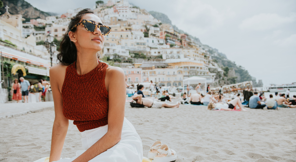 Lady sitting on beach in italy with cliff full of buildings in background