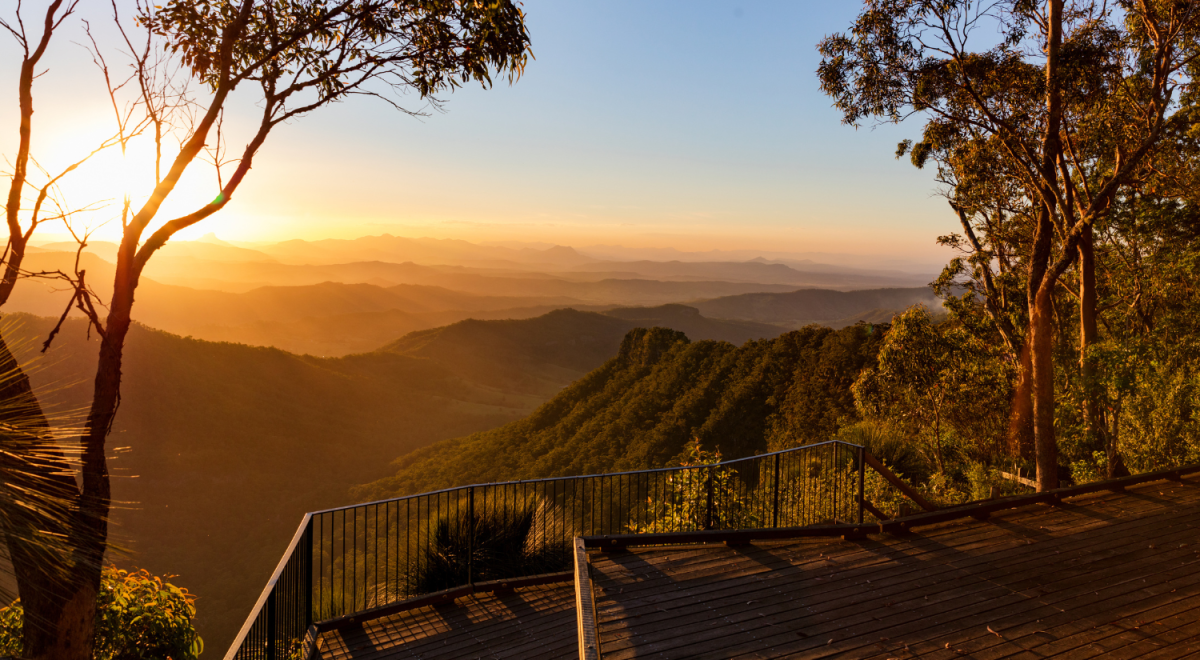 Golden sunset over rolling mountain ranges viewed from a timber lookout deck in the Gold Coast Hinterland with eucalyptus trees framing the glowing sky