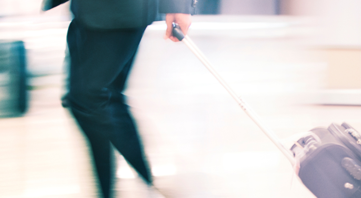 A man rushing through the airport with a carry-on in tow