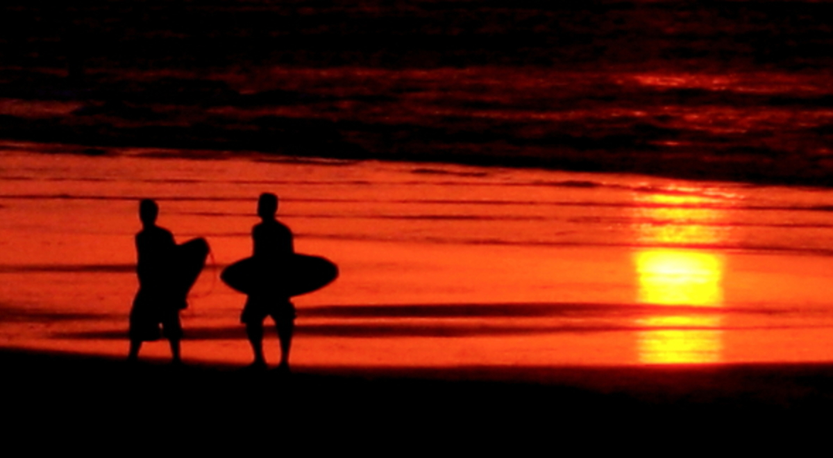 a silhouette of two men carrying their surfboard across the shore during late sunset