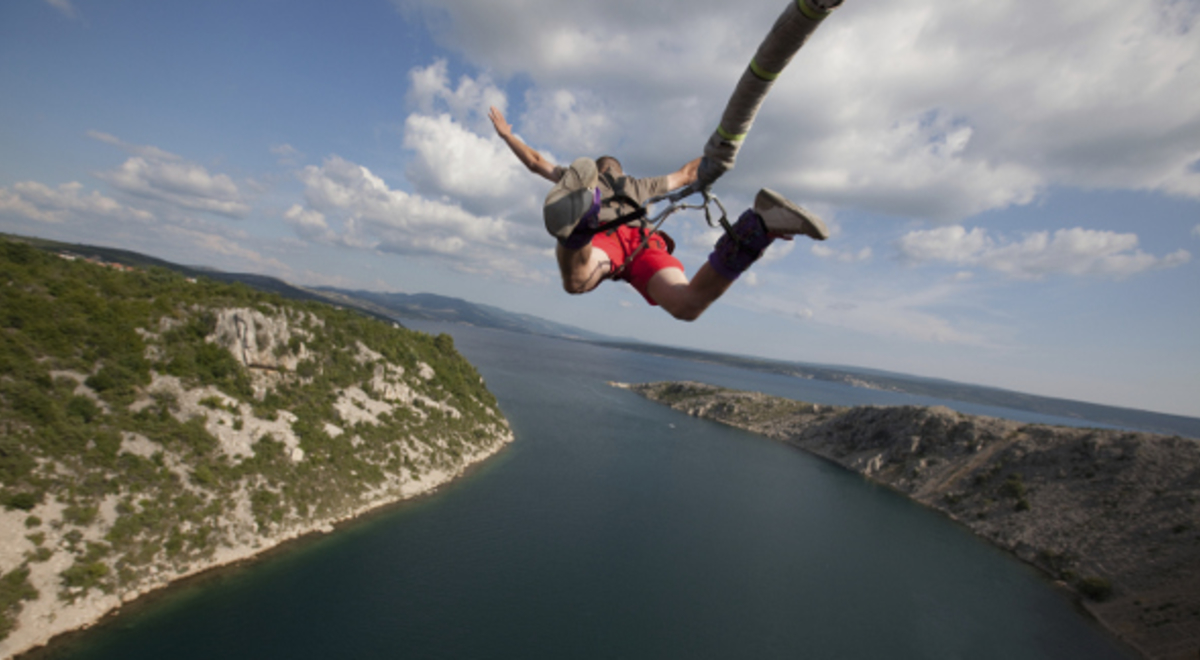 aerial view of a person in red shorts bungee jumping over a river