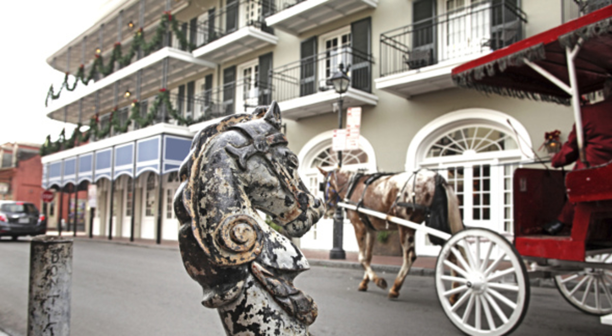 A horse pulling a red carriage in front of a horse statue