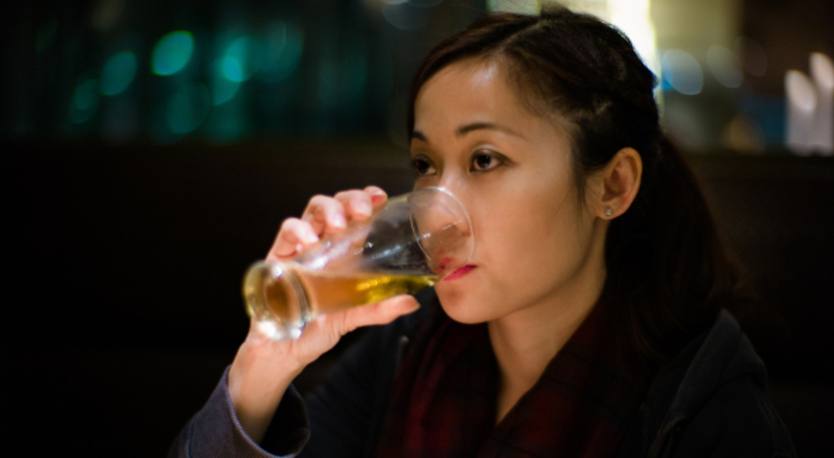 Woman with dark hair drinking a beer 