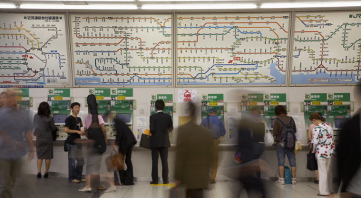 People moving in a busy public transport station in front of a colour-coded map