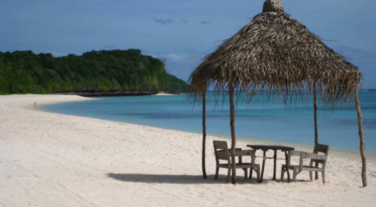 a small hut on the shore of the ocean and underneath it is a small wooden table with two wooden chairs