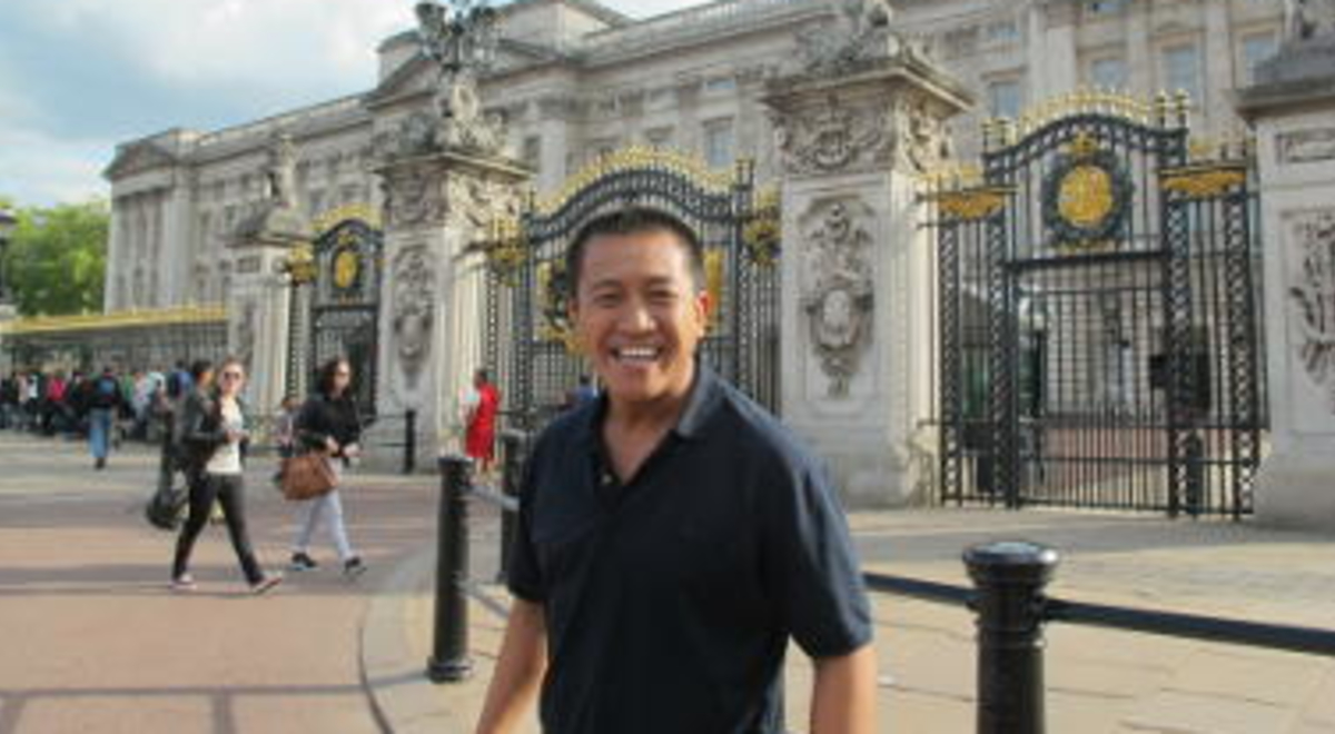 Anh Do standing in front of Buckingham Palace