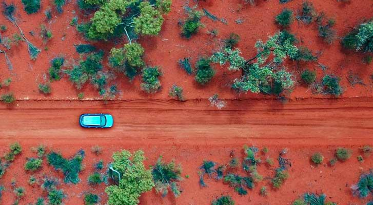Car driving through the red roads of Alice Springs surrounded by green trees