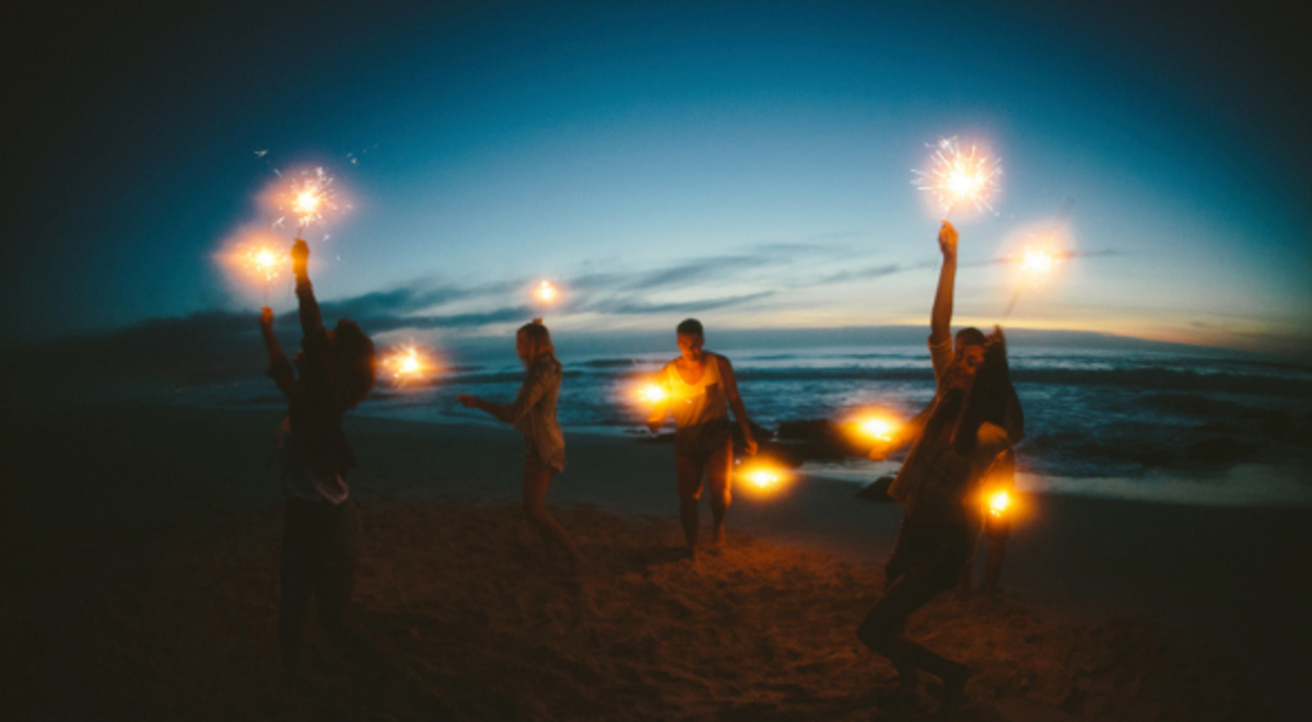 friends happily lighting firework sparklers on the beach at night