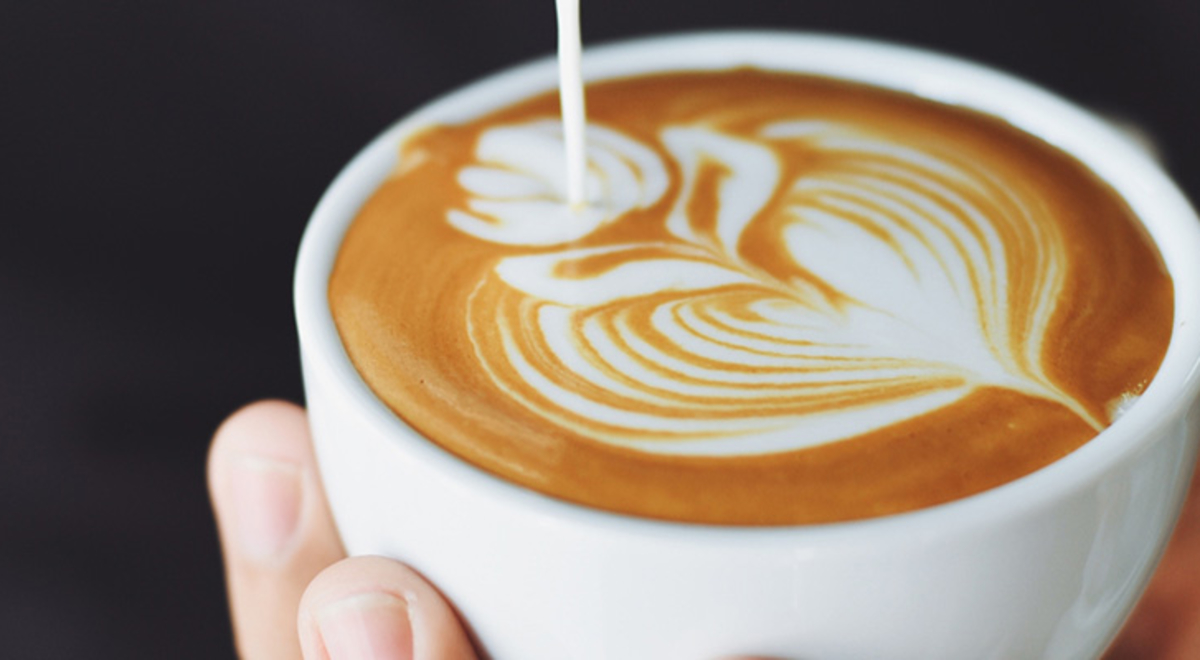 a leaf with heart coffee art on a small white cup
