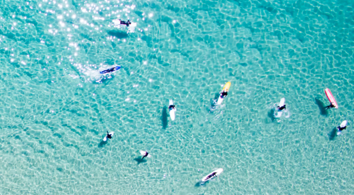 Aerial view of surfers on clear blue beach waters.