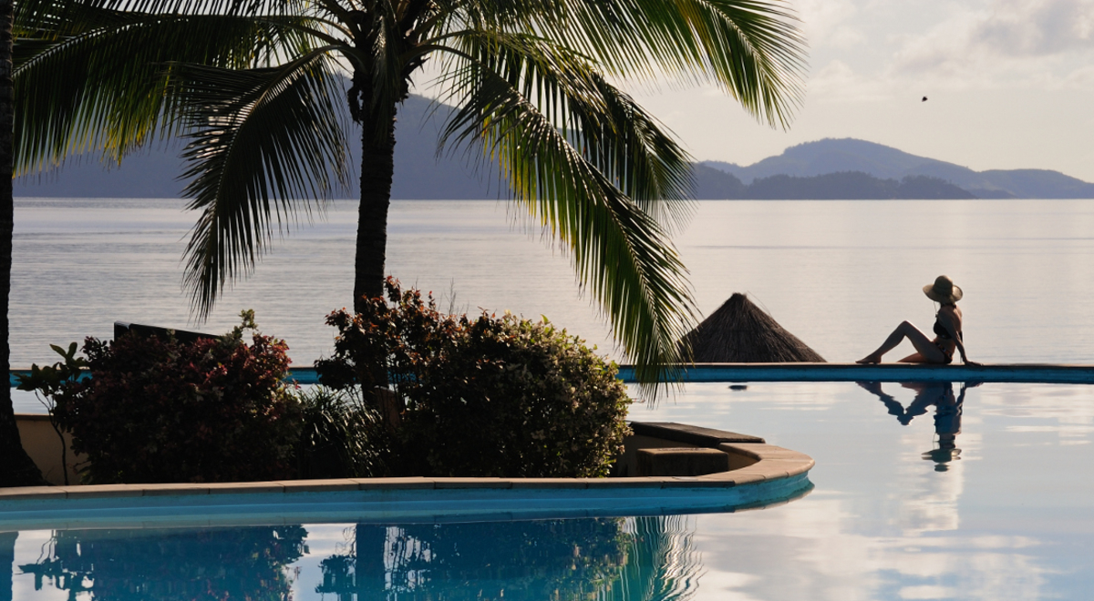 Woman sitting on the edge of the pool at a beachfront resort as the sun goes down at Hamilton Island.