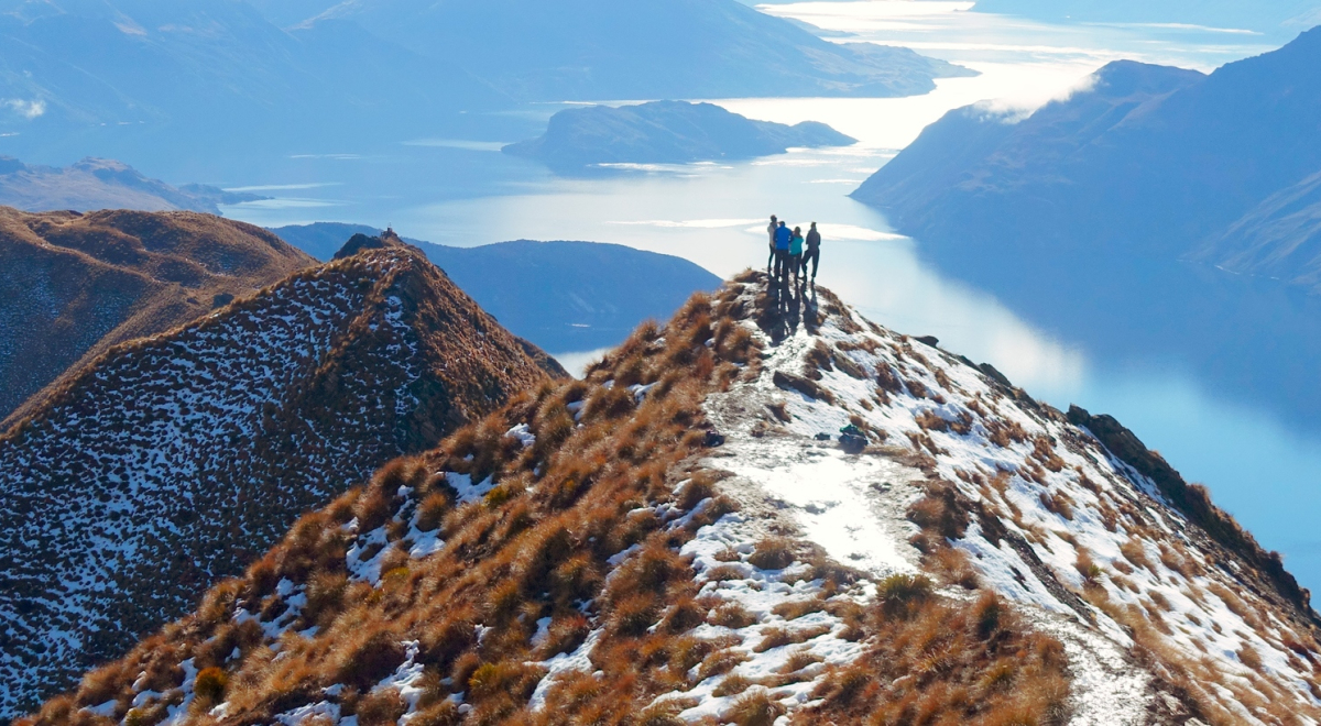 Distant view of hikers standing on a cliff against lake during winter, Queenstown
