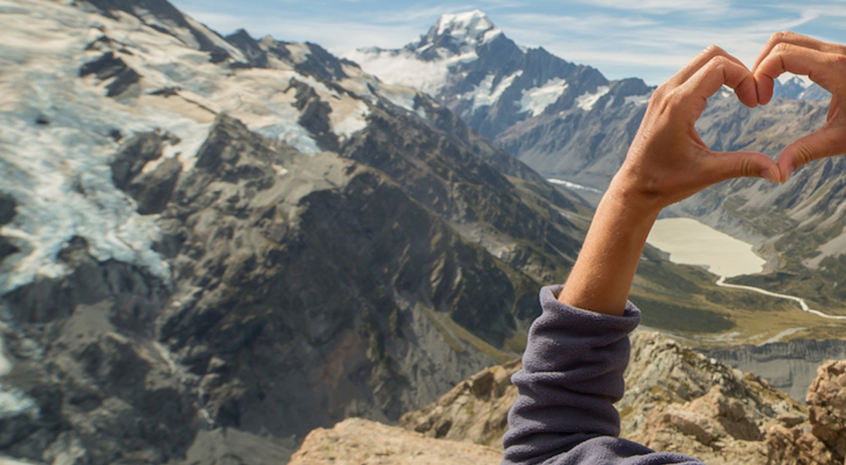 Woman looking towards the mountains making the shape of a heart with her hands 