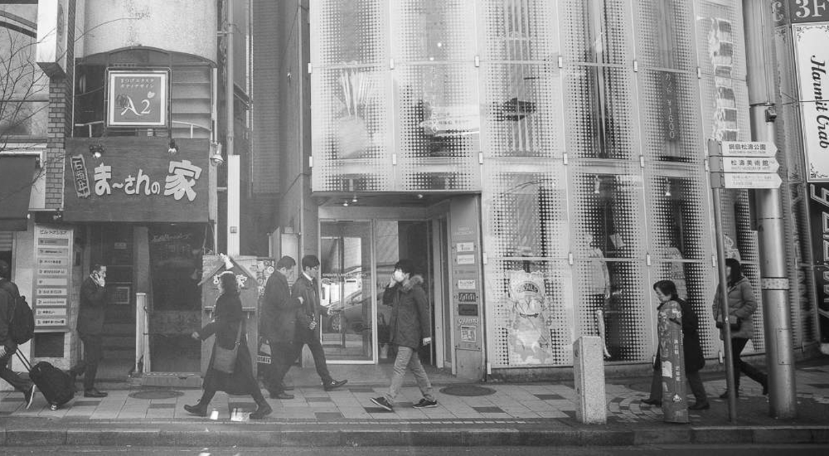 Black and white photo of pedestrians walking past the buildings in Tokyo