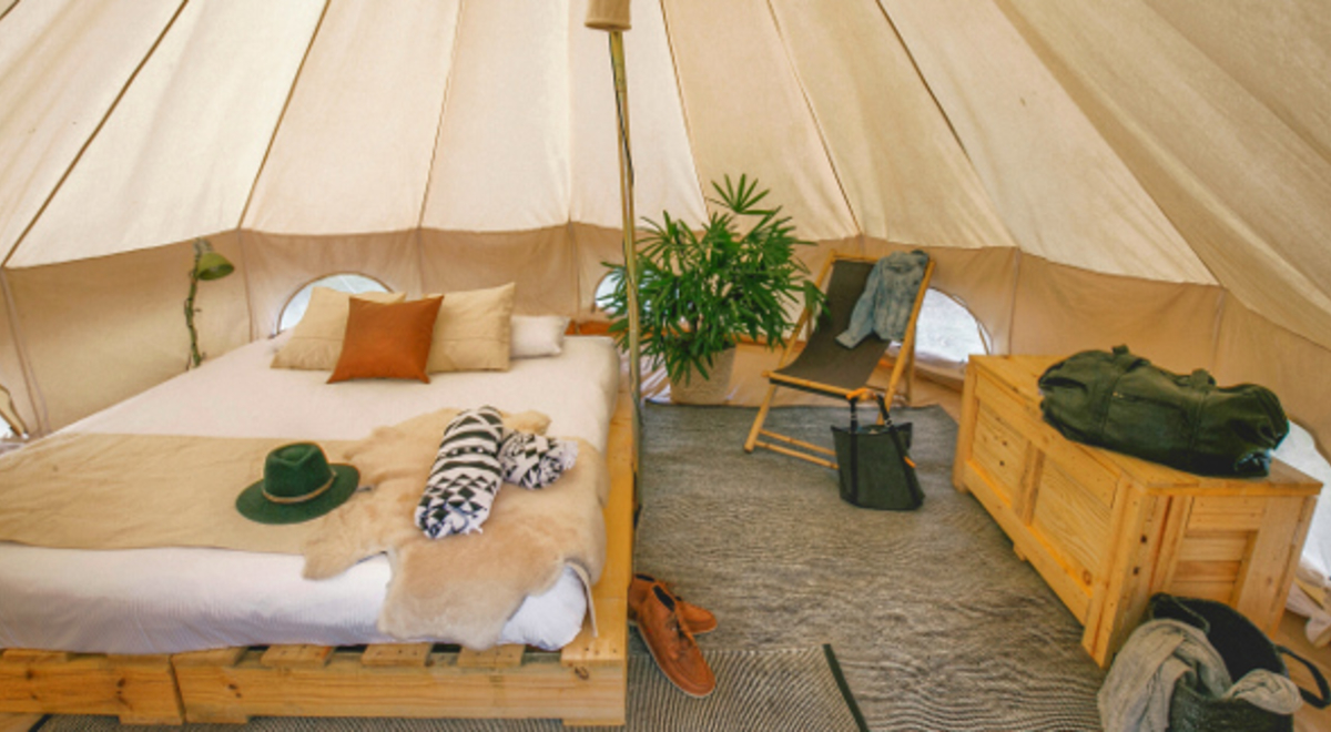 Interior of a large, beige tent with a bed, char and chest of drawers inside